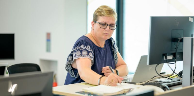A woman working in front of computer screens wearing glasses
